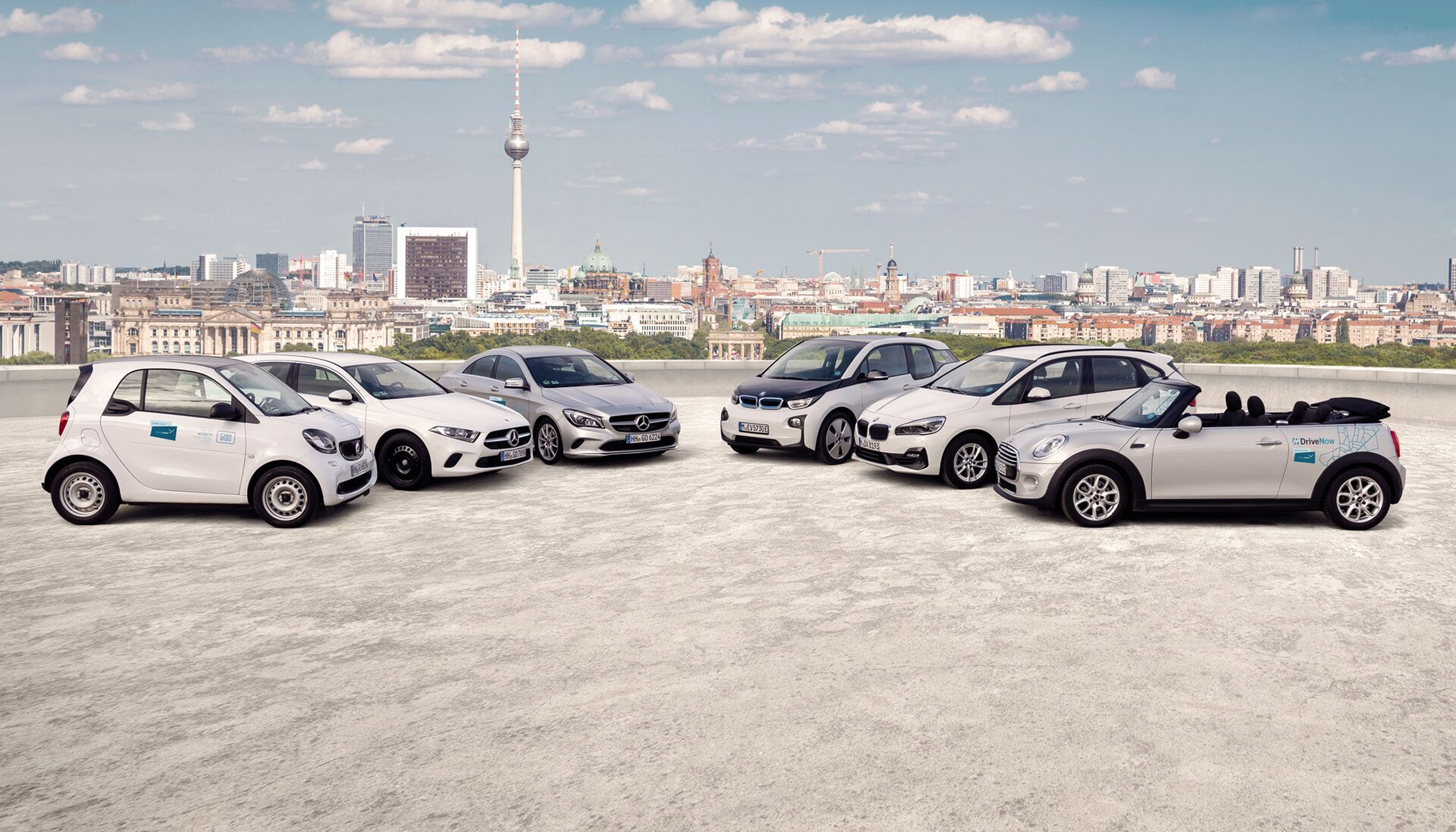 Share Now fleet lineup in Berlin — Smart Fortwo, Mercedes A-Class, BMW i3 and MINI parked in front of the Berlin skyline and TV tower