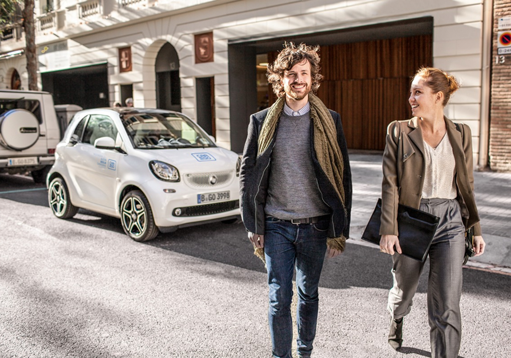 A couple walking down a Berlin street next to a car2go Smart Fortwo